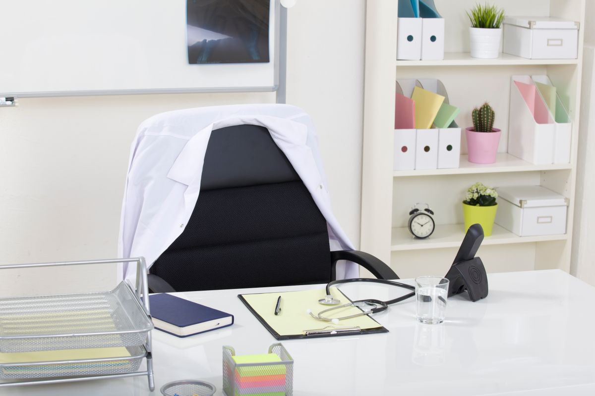 An empty office desk holds a stethoscope and clipboard in front of a chair.