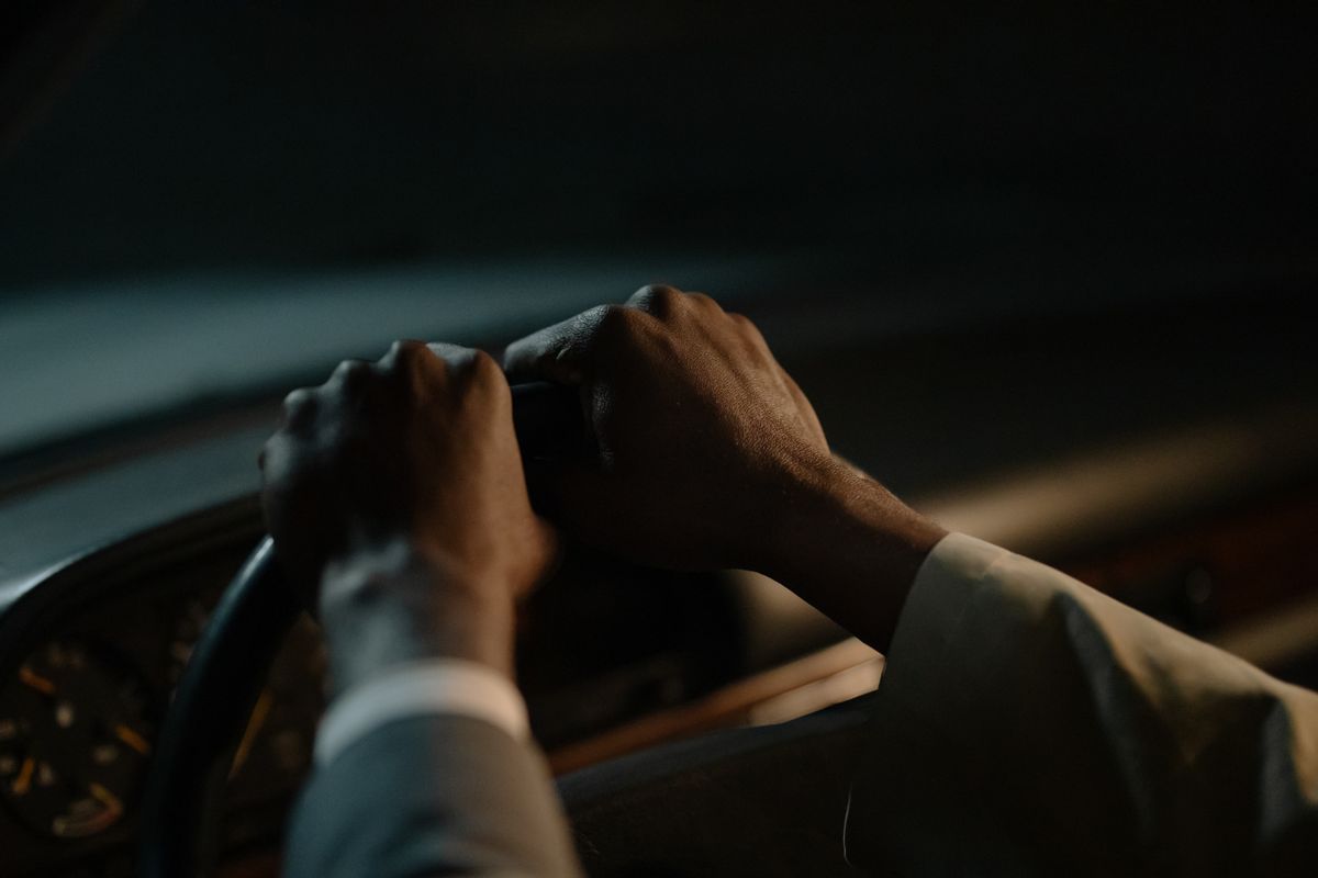 Two hands hold a steering wheel inside a dimly lit car.